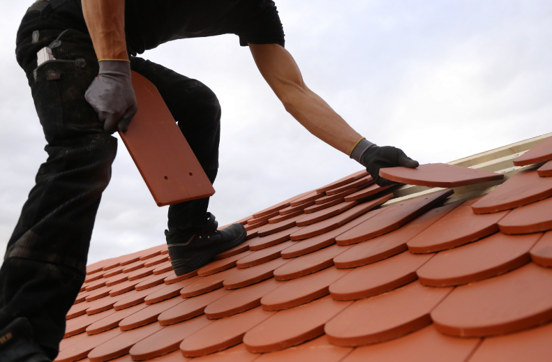 A roofing contractor adding new tiles to the roof